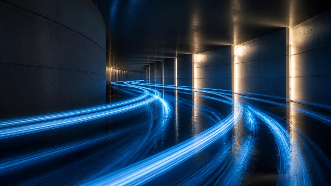 Blue light trails sweeping through an illuminated concrete corridor in a long exposure